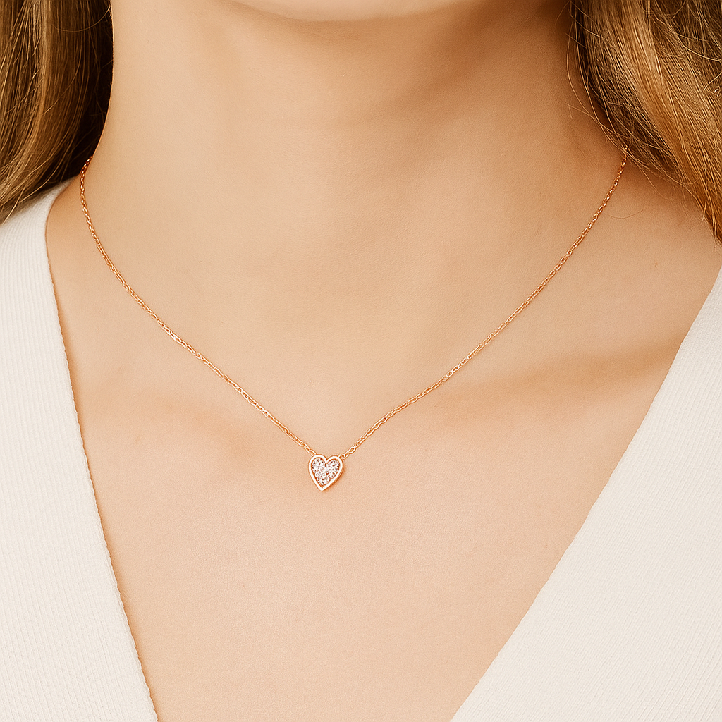 Rose gold necklace with a heart-shaped pendant on a person wearing a white top.