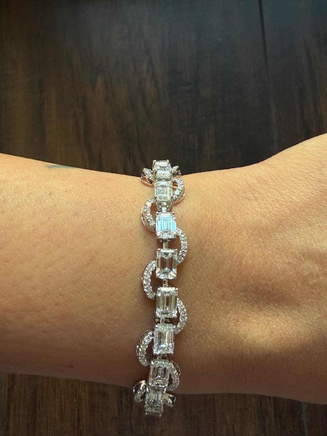 Silver bracelet with rectangular gemstones on a wrist against a wooden background