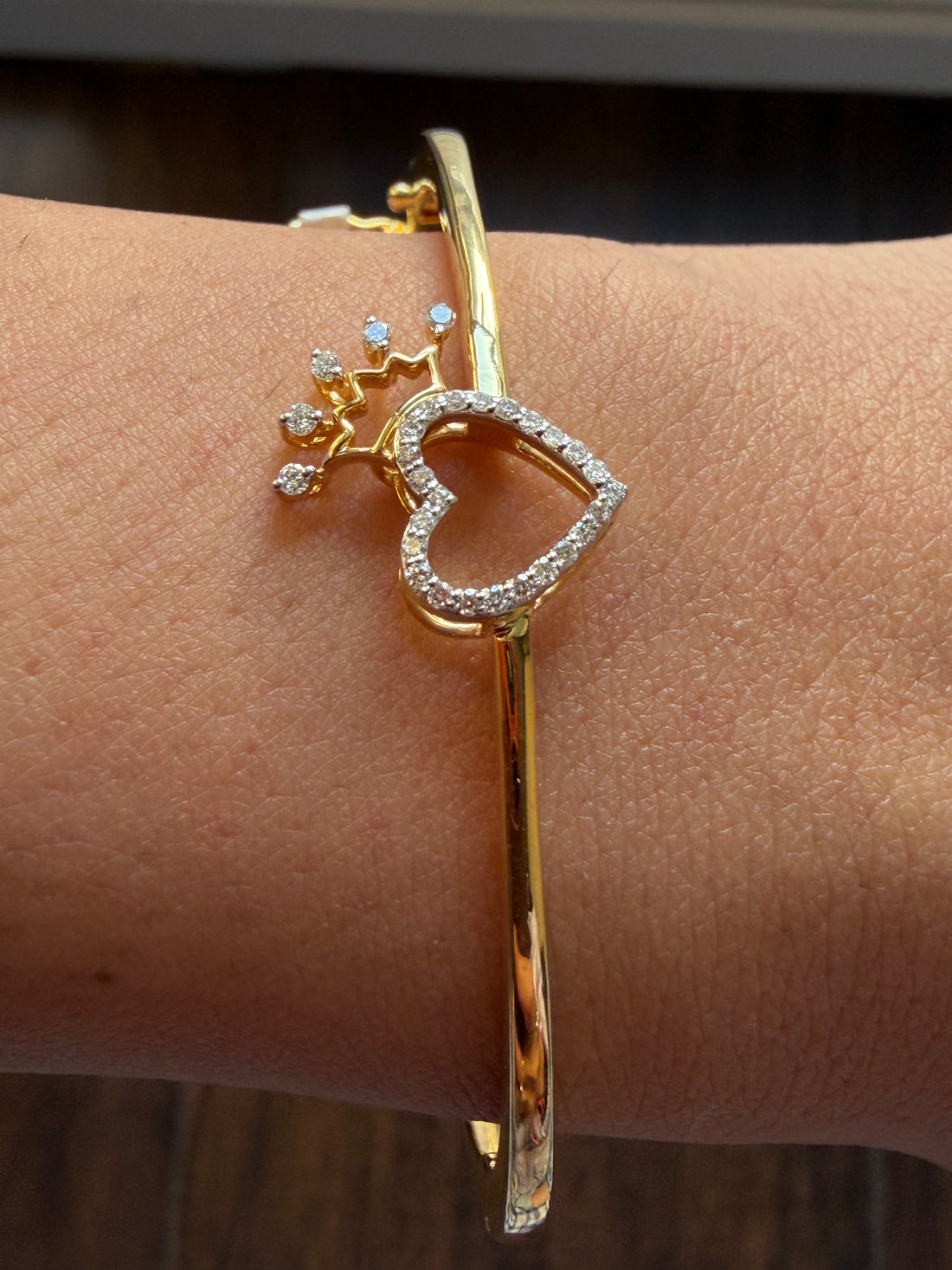 Gold bracelet with heart and star design on a wrist against a neutral background