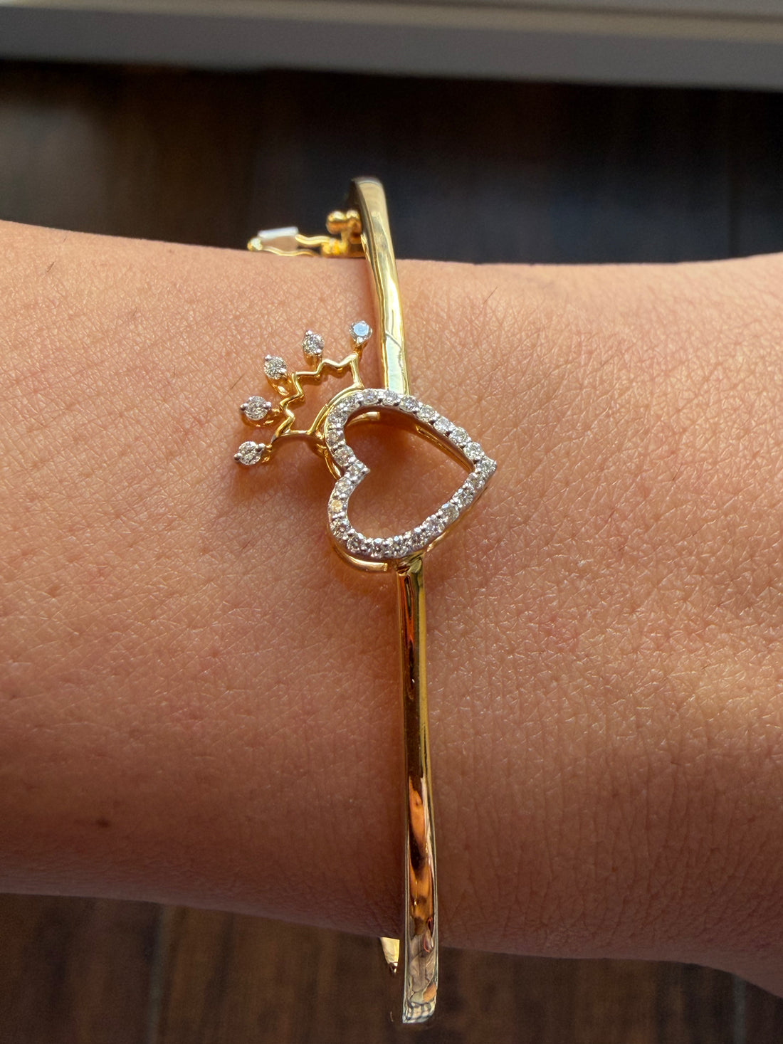 Gold bracelet with heart and diamond design on a wrist against a blurred background