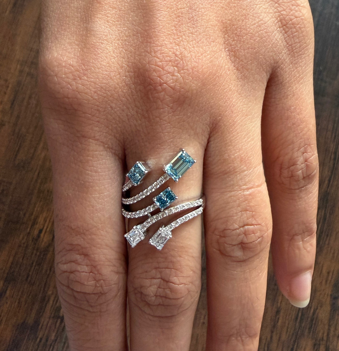 Silver ring with blue gemstones on a person's finger against a wooden background