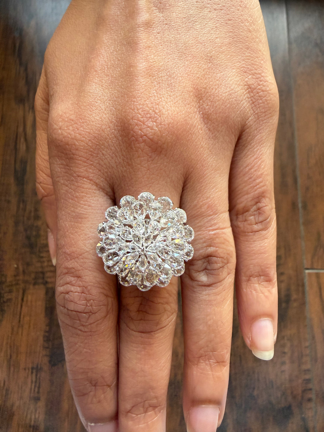 Silver ring with a floral design on a person's finger against a wooden background