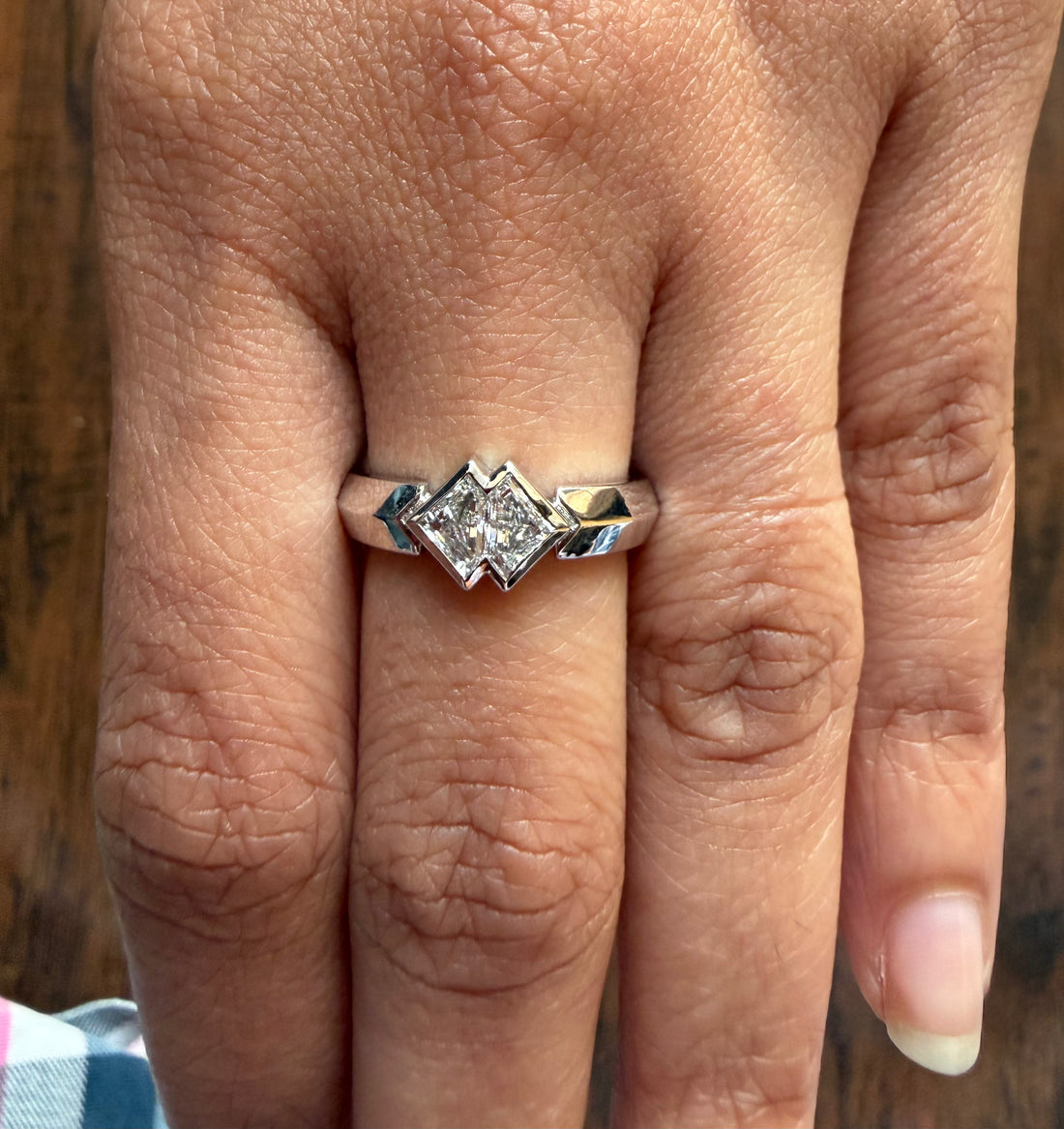 Silver ring with a diamond on a person's finger against a wooden background