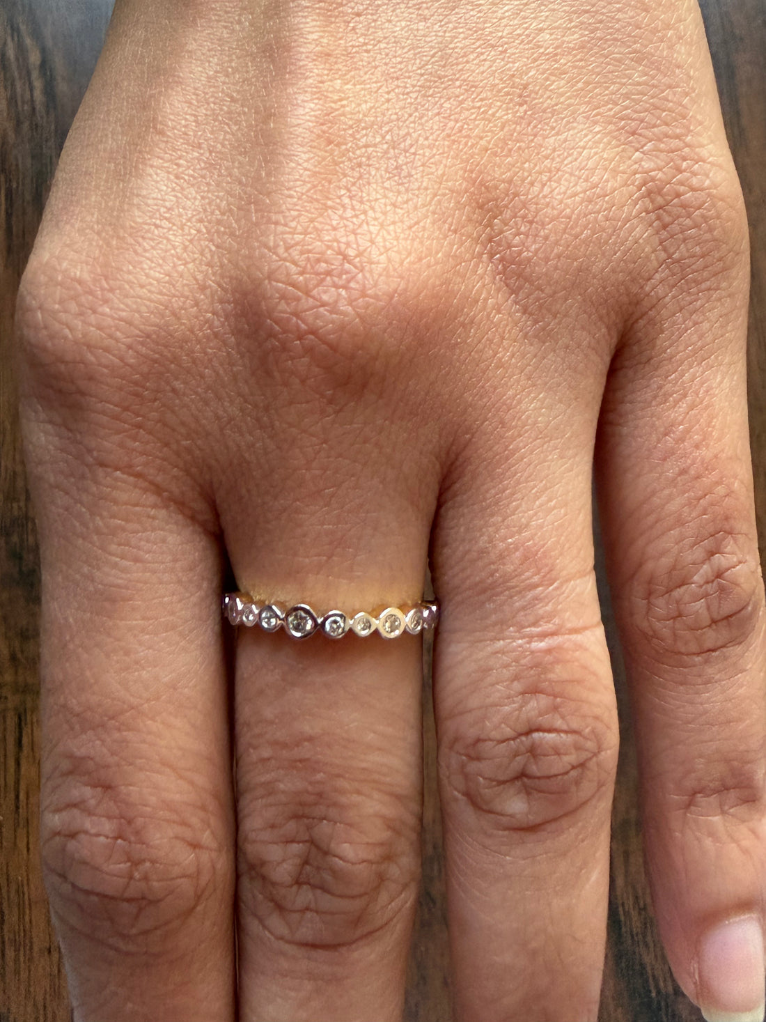 Close-up of a hand wearing a gold ring with small stones on a wooden background