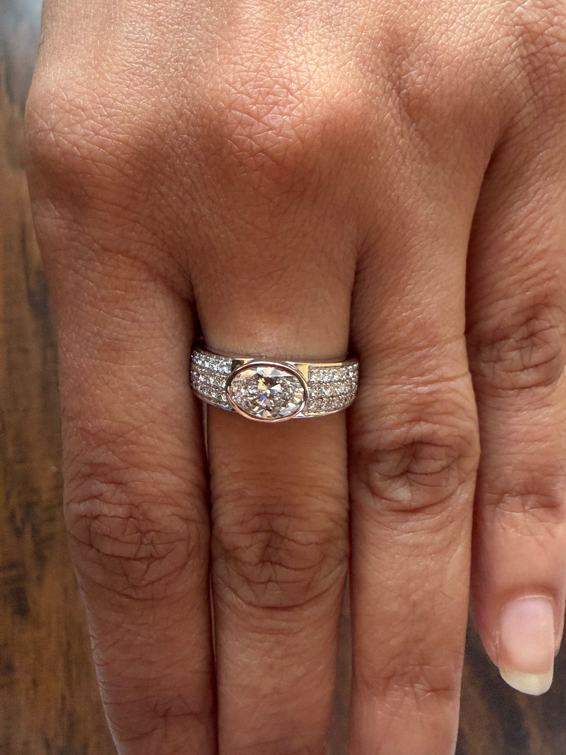 Close-up of a hand wearing a diamond ring on a wooden surface