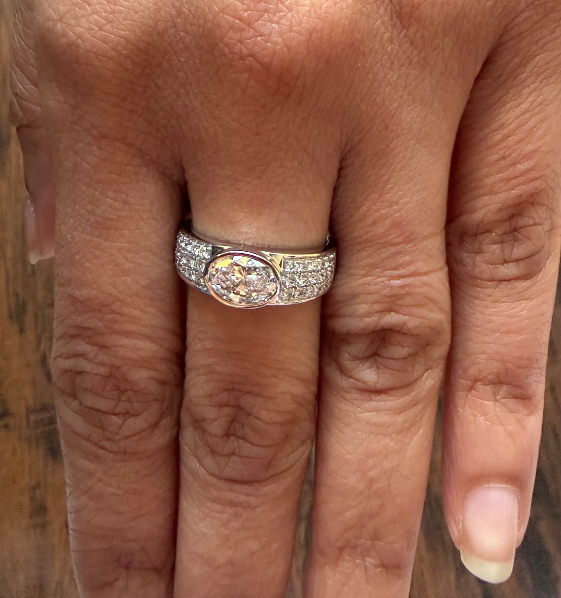 Close-up of a hand wearing a silver ring with a large gemstone on a wooden surface.