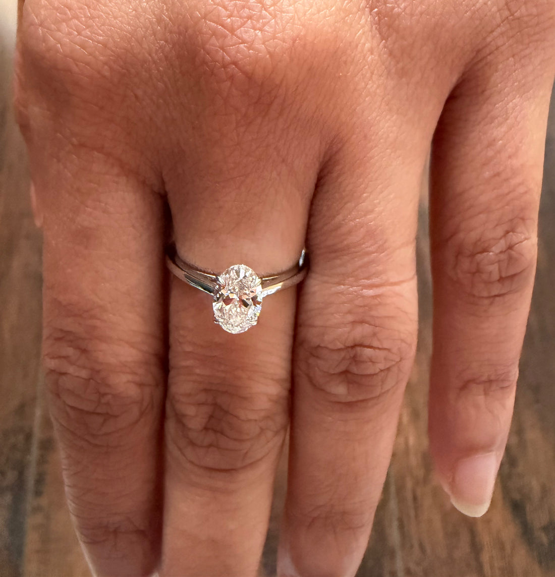 Silver ring with a diamond on a person's finger against a neutral background
