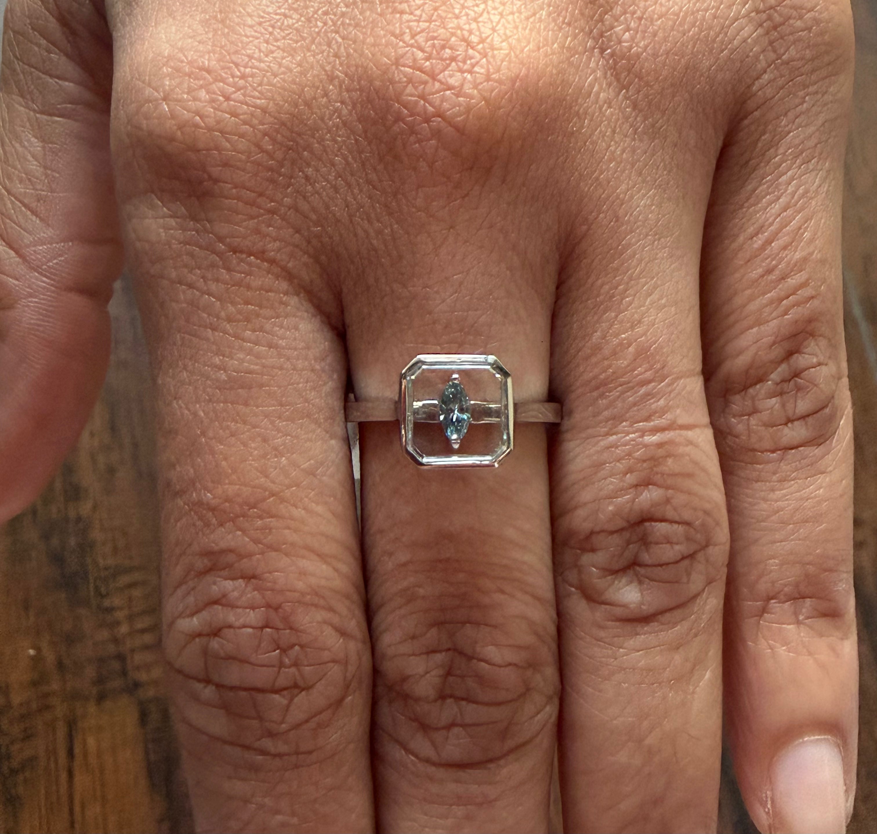Close-up of a hand wearing a silver ring with a gemstone on a wooden surface