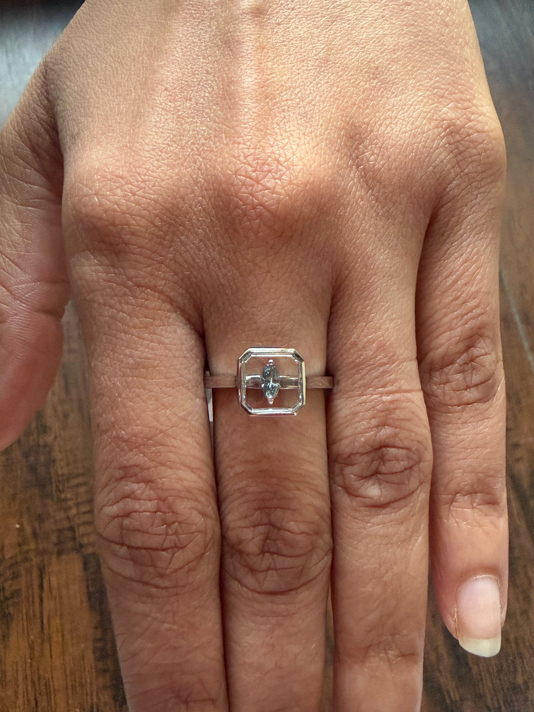 Close-up of a hand wearing a silver ring with a diamond on a wooden surface