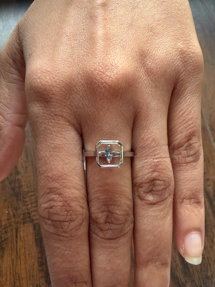 Close-up of a hand wearing a silver ring with a diamond on a wooden surface