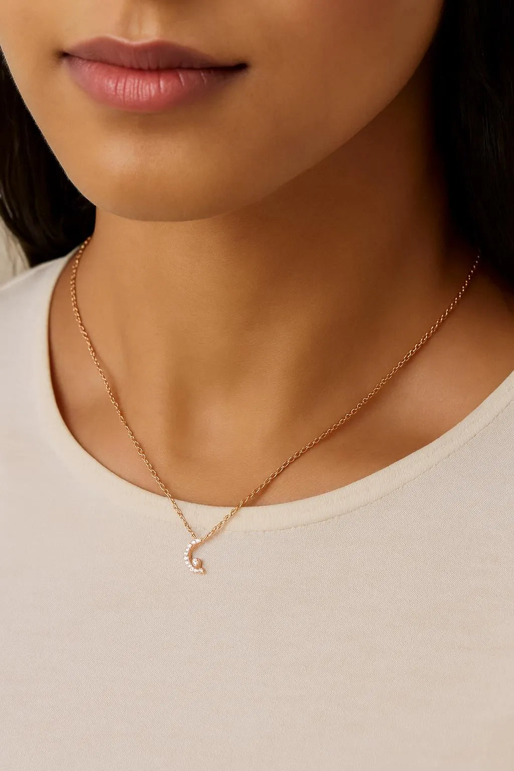 Close-up of a person wearing a delicate gold necklace on a plain background